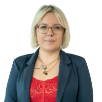 Professional headshot of a blonde woman in a blue blazer and red lace top, wearing glasses.