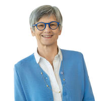 Portrait of a smiling woman with short gray hair wearing blue-framed glasses, a white blouse, and a blue cardigan.