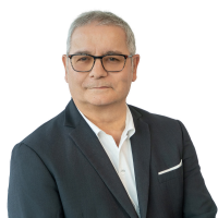 Portrait of a middle-aged man in a dark suit, white shirt, and glasses, looking at the camera against a white background.