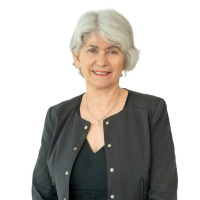 Professional headshot of a smiling older woman with short gray hair, wearing a black blazer and necklace.