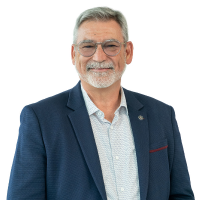 Professional portrait of a smiling older man with gray hair and beard wearing a blue blazer and light shirt.