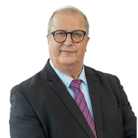 Professional headshot: middle-aged man with gray hair and glasses, wearing a dark suit, light blue shirt, and pink striped tie.