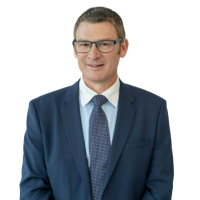 Professional headshot of a man in a navy suit and tie with glasses against a white background.
