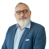 Professional portrait of a mature man with glasses and a white beard, wearing a blue blazer and light blue shirt, looking at the camera.