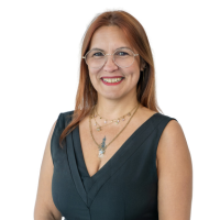 Portrait of a smiling woman with light brown hair and glasses, wearing a dark green sleeveless top and a necklace.
